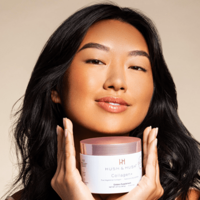 Woman holding the new Hush & Hush Collagen+ Product. Product in a white tub with a rose gold lid. Photo has a gradient beige background